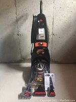 Front view of upright Bissell shampooer with cleaning brush attachments and user manual placed on floor in front of unit.