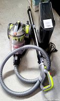 Hoover vacuum cleaner body with hose and wand, and Oreck air purifier in background on floor