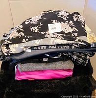 Stack of various folded ladies clothing including floral prints, knits, and bright colored items.