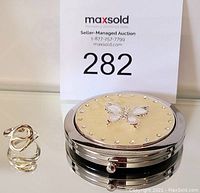 Photo showing sterling silver double-loop ring and round mirrored compact with gold butterfly-decorated lid