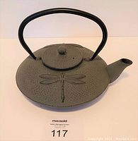 Photo showing closed teapot with visible dragonfly imprint on body and lid, black handle.