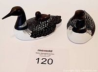 Photo displaying two ceramic loon figurines, one with a small chick on its back, both painted black and white with spotted feather patterns.