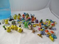Overview of assortment of approximately 45 colorful plastic Pokemon figurines from Kinder Surprise, spread out on a white cloth background.