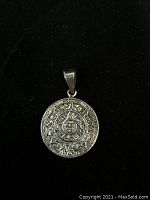 Front side of the pendant showing detailed Aztec calendar design in silver relief on black background.