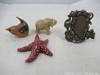 View of all four items in the lot: ceramic bird, stone elephant, red ceramic starfish, and metal picture frame.