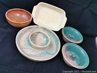 Overview photo showing six art pottery ceramic pieces including a large round divided platter with a central dip bowl, two blue-green and brown ring holder dishes, one reddish brown bowl, and one speckled rectangular shallow dish.