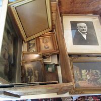 Overview photo of assorted vintage framed pictures and paintings packed inside a wooden box.