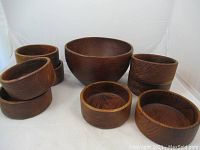 Full view showing one large wooden bowl with nine smaller wooden bowls stacked and arranged around it, all have a dark wood finish.