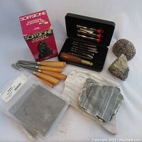 Full lot overview showing boxed Sofstone soapstone sculpture kit, chisels, carving bits in black case, soapstone rocks, and slate.
