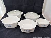 Front view of five vintage CorningWare casserole dishes with Blue Cornflower pattern, two with glass lids.