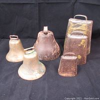 Seven vintage and antique bells in various sizes showing signs of rust, oxidation, and paint remnants on a dark background.