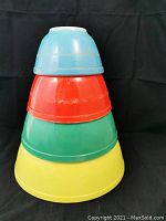 Stack of four vintage Pyrex mixing bowls in yellow, green, red, and blue colors.