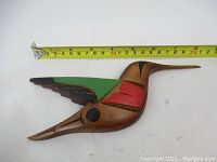 Wooden hummingbird plaque measured with tape at 8 inches long, showing the full front side with color painted wing.