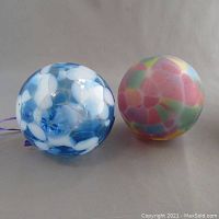 Two blown art glass baubles side by side on a neutral background showing color and pattern details.