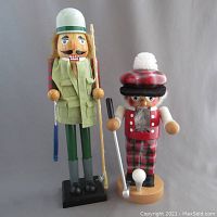 Front view of two nutcracker figurines, one golfer-themed and one Scottish-themed with plaid clothing and golf equipment.