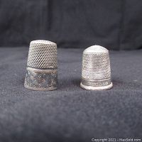 Two vintage silver thimbles side by side on black cloth background, showing overall condition and comparison in size and design.