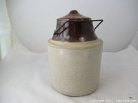 Front view of vintage Medalta ceramic pickling canister with cream base and brown lid with metal handle.