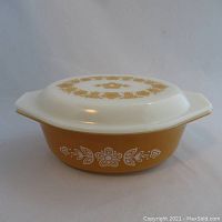 Side view of vintage PYREX casserole dish with lid showing orange base and white floral pattern