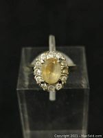 Top view of vintage women's ring featuring an oval yellow cabochon gemstone surrounded by smaller clear stones in a silver setting.