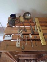 All items displayed on wooden bench: serving ladle, serving spoon, two forks, five small spoons, salt cellar and mustard pot.