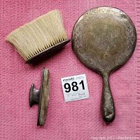 Three items: a hand mirror, a makeup brush with broken handle, and the brush detached handle piece on pink cloth