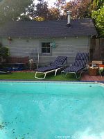 Photo showing two adjustable chaise loungers with navy blue striped cushions set up near a pool in front of a shed.
