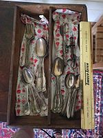 Wooden trays filled with assorted tarnished silver flatware pieces including forks, spoons, and some black-handled utensils.