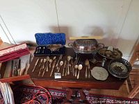 Assorted silver plated flatware and serveware on wooden table