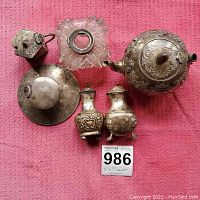 All items arranged on pink cloth: teapot, salt & pepper shakers, inkwell, candle holder, wick trimmer
