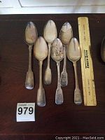 Six spoons laid flat next to 12-inch ruler on dark wood surface