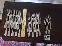 Wide view of all 14 silver forks arranged in two groups with a ruler for scale