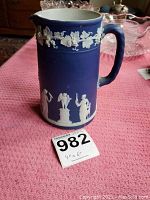 Side view of the Wedgwood blue jasperware pitcher showing white relief figures and grapevine motif near rim.
