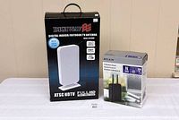Photo showing boxed Digiwave Digital Indoor/Outdoor TV Antenna and boxed Belkin N300 wireless router placed side by side on a wooden surface against a plain background.