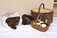 Photo showing large wicker basket with wooden liner, smaller wicker basket with handle, two bags of pine cones, and decorative birds and flowers arranged together.