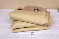 Folded curtain panels showing beige textured fabric with muted brown faux suede top and silver metal grommets.