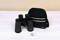 Binoculars, lens caps, and carry bag displayed on a white cloth with a tag