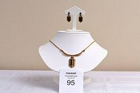 Necklace and matching earrings displayed on a white jewelry mannequin stand against a beige background. Necklace is gold colored with a central Tigers Eye stone surrounded by Swarovski crystals, approximately 18" chain length. Earrings dangle with Tigers Eye stones and crystals.