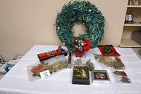 Photo showing turquoise wreath, red and gold ribbons, silver door hanger, metal Christmas pail, Snow Babies bisque ornament, and assorted Christmas decorations arranged on table.