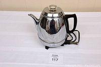 Silver electric coffee percolator on white table with removable cord and black handle, photographed for listing.