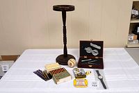 Photo of entire lot on table includes wooden ashtray stand, boxed men's gift set, signed baseball, pens, watch, mini checkers game, and pins.