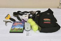 Photo showing all dog-related items in the lot: nail clippers, brushes, black direct seat belt tether, knapsack, three tennis balls, dog training DVD, and flea and tick fobs.