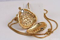 Gold-coloured necklace with a purse-shaped pendant featuring Aurora Borealis Swarovski Crystals, shown open to display interior and magnetic clasp.