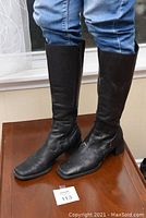 Black knee high leather boots being worn, showing shaft length up to knee and block heel.