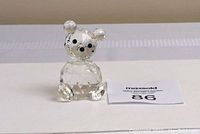 Clear faceted Swarovski crystal bear figurine with black eyes and nose, sitting upright on a white surface with a MaxSold lot number card.