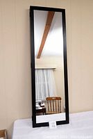 Full length mirror with black frame standing upright against wall, showing reflective surface and simple design.