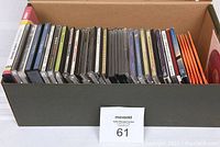 Box of various music CDs and DVDs shown from top with cases and sleeves visible.