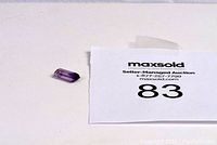 Single natural amethyst gemstone placed on a flat white surface beside a paper tag marked with auction lot number 83 and MaxSold branding.