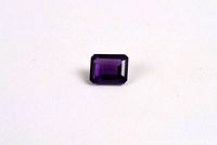 Top-down view of a deep purple emerald cut amethyst gemstone on a white surface.