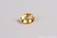Oval citrine gemstone laying flat showing cut and color.