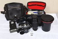 Full lot showing two cameras, lens, film developing tank, bags, filters, flash unit, batteries, accessories on white background